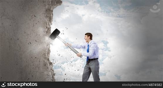 Businessman with hammer. Young determined businessman with big hammer in hands crashing wall