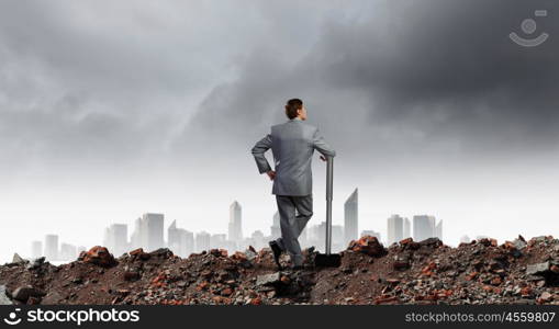 Businessman with hammer. Young determined businessman with big hammer in hands standing on ruins