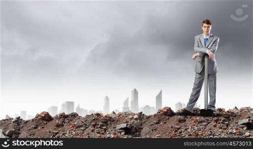 Businessman with hammer. Young determined businessman with big hammer in hands standing on ruins