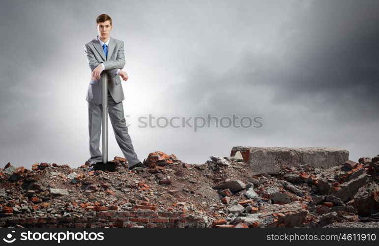 Businessman with hammer. Young determined businessman with big hammer in hands standing on ruins