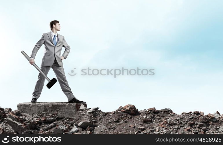 Businessman with hammer. Young determined businessman with big hammer in hands standing on ruins