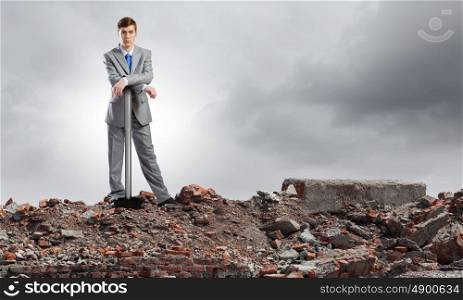 Businessman with hammer. Young determined businessman with big hammer in hands standing on ruins