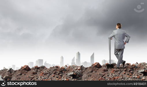 Businessman with hammer. Young determined businessman with big hammer in hands standing on ruins