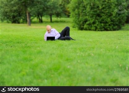 Businessman with laptop lying on green grass in the park
