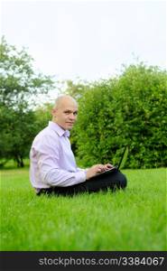 Businessman with laptop on the green grass in the park