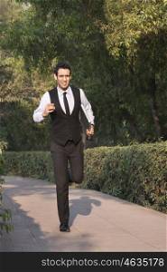 Businessman with laptop running in a park , INDIA , DELHI