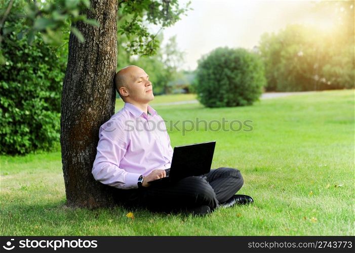 Businessman with laptop sitting near a tree in the park