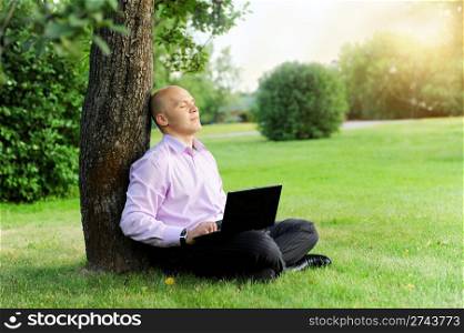 Businessman with laptop sitting near a tree in the park