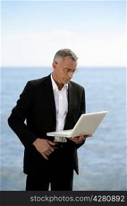 Businessman with laptop stood by lake