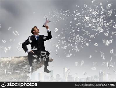 Businessman with megaphone. Young businessman on top of rock screaming in megaphone