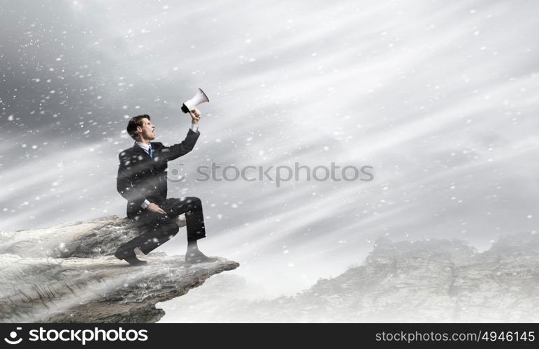 Businessman with megaphone. Young businessman on top of rock screaming in megaphone