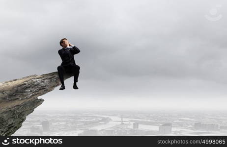 Businessman with megaphone. Young businessman on top of rock screaming in megaphone