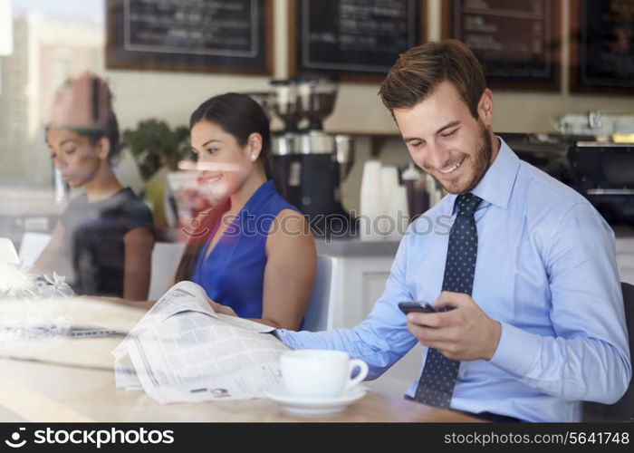 Businessman With Mobile Phone And Newspaper In Coffee Shop