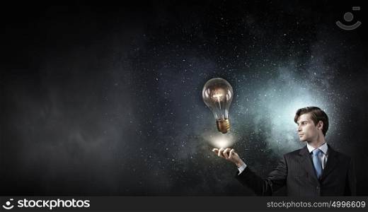 Businessman with mobile phone. Young businessman with mobile phone in hand looking at glass lightbulb