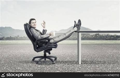 Businessman with mug. Young confident businessman sitting in chair with mug in hands