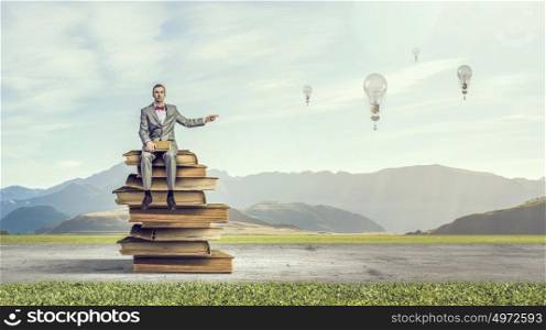 Businessman with old book. Young businessman sitting on pile of books and pointing with finger