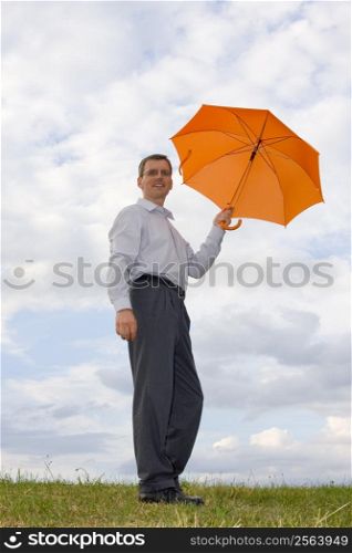 Businessman with orange umbrella in a meadow
