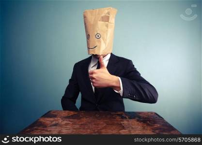Businessman with paper bag over his head giving thumb up
