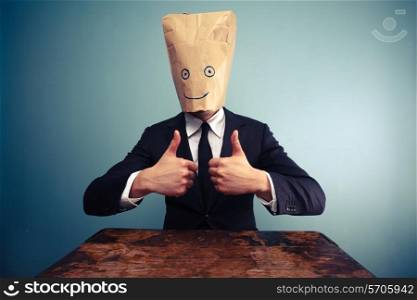 Businessman with paper bag over his head giving thumbs up