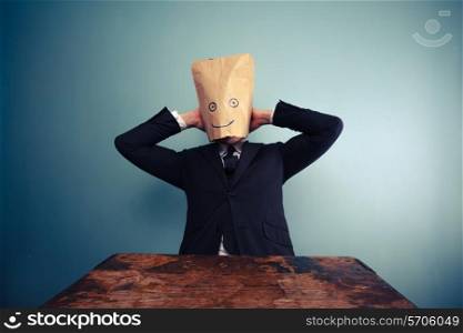 Businessman with paper bag over his head relaxing at desk