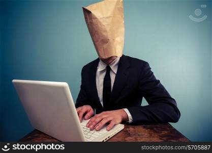Businessman with paper bag over his head working on laptop