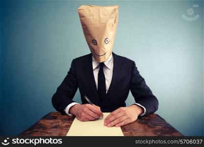Businessman with paper bag over his head writing at desk