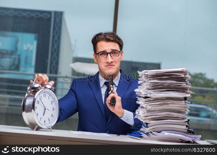 Businessman with pile stack of paper paperwork and an alarm cloc. Businessman with pile stack of paper paperwork and an alarm clock working in the office