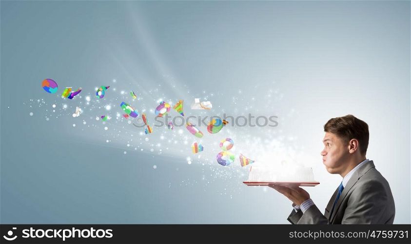 Businessman with red book. Young businessman blowing on opened book and infographs flying from pages