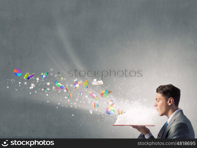 Businessman with red book. Young businessman blowing on opened book and infographs flying from pages