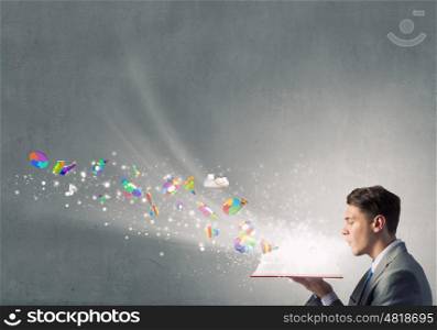 Businessman with red book. Young businessman blowing on opened book and infographs flying from pages