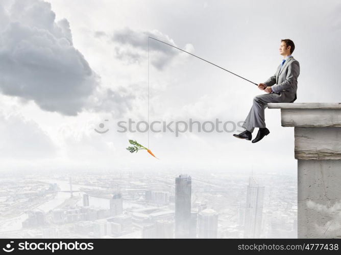 Businessman with rod. Young businessman sitting on top of building and fishing