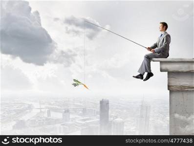 Businessman with rod. Young businessman sitting on top of building and fishing