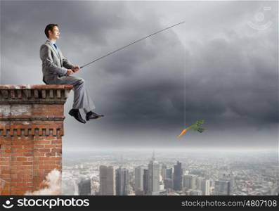 Businessman with rod. Young businessman sitting on top of building and fishing