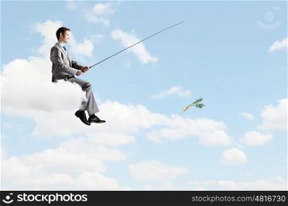 Businessman with rod. Young businessman standing on cloud high in sky and fishing