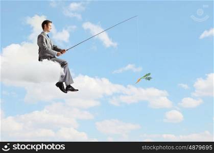 Businessman with rod. Young businessman standing on cloud high in sky and fishing