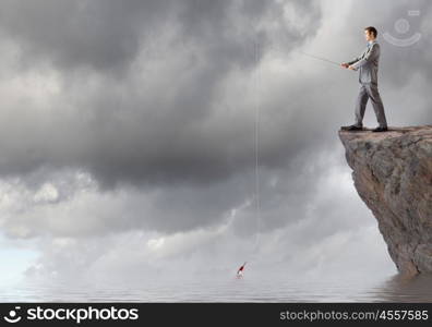 Businessman with rod. Young businessman standing on top of rock and fishing