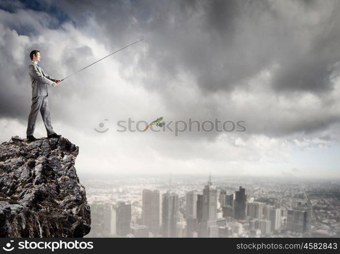 Businessman with rod. Young businessman standing on top of rock and fishing