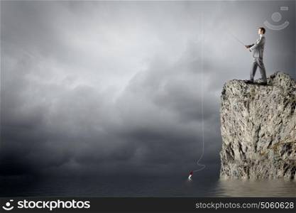Businessman with rod. Young businessman standing on top of rock and fishing