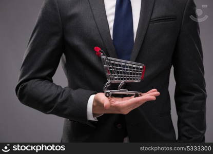 Businessman with shopping cart on gray background