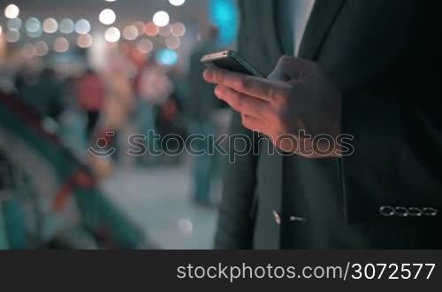 Businessman with smart phone at the airport. He typing sms or email on touchscreen. Defocused crowd in background