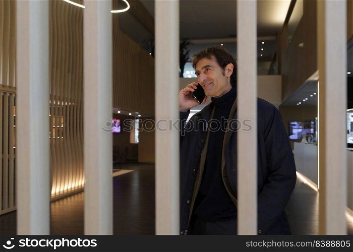 Businessman with smartphone by ear while entering hall of contemporary hotel and calling colleague