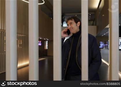 Businessman with smartphone by ear while entering hall of contemporary hotel and calling colleague