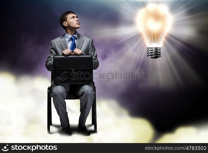 Businessman with suitcase. Businessman sitting on chair and looking on light bulb