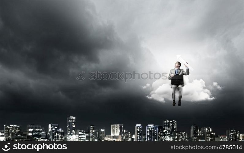 Businessman with suitcase. Young smiling businessman sitting on cloud with arrow in hands
