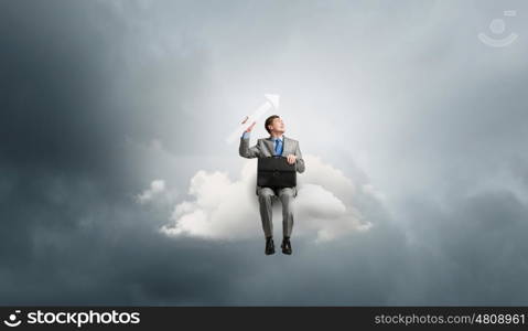 Businessman with suitcase. Young smiling businessman sitting on cloud with arrow in hands