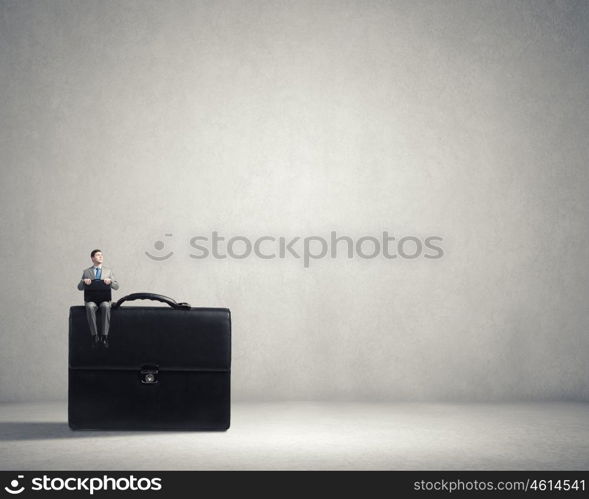 Businessman with suitcase. Young smiling businessman sitting on giant briefcase