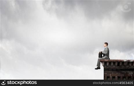 Businessman with suitcase. Young smiling businessman sitting on top with briefcase in hands