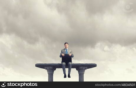 Businessman with suitcase. Young smiling businessman sitting on top with briefcase in hands