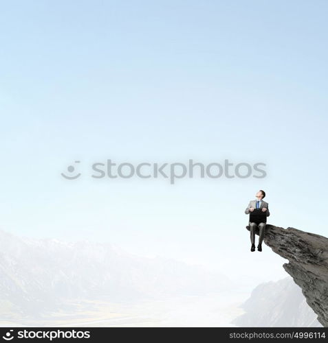 Businessman with suitcase. Young smiling businessman sitting on top with briefcase in hands