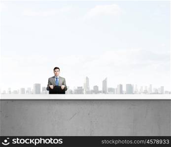 Businessman with suitcase. Young smiling businessman sitting with briefcase in hands